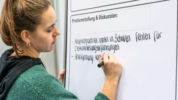 Eine Teilnehmerin schreibt politische Forderungen auf ein Flipchart.