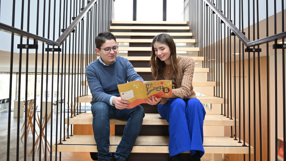 Die FSJ-ler Julian und Leonie sitzen auf einer Treppe im Plenargebäude und tauschen sich zu einer Publikation aus.