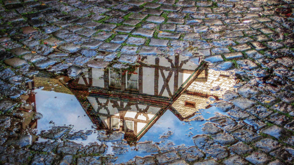 Fachwerkhausspiegelung in Pfütze und Kopfsteinpflaster