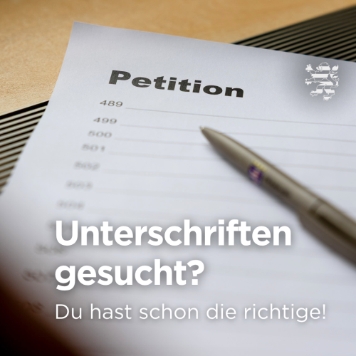 Auf einem Holztisch liegt ein weißes Blatt mit der Überschrift „Petition“ und einer einzelnen Unterschrift in blauer Tinte. Daneben liegt ein schwarzer Kugelschreiber. In der unteren Bildmitte steht: "Unterschriften gesucht? Du hast schon die richtige!"