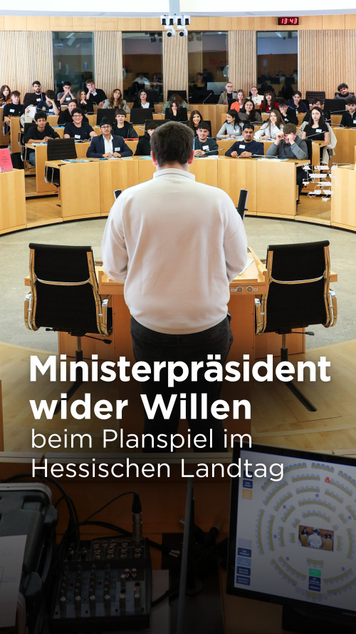 Der Plenarsaal des Landtages ist im Bild zu sehen. Im Vordergrund befindet sich ein Mikrofon, auch die Redezeitanlage im Sitzungssaal ist auf einem Bildschirm zu erkennen. Am Rederpult befindet sich ein Jugendlicher, der an einem Planspiel teilnimmt. Vor ihm sind weitere Schülerinnen und Schüler zu erkennen, die auf den Sitzplätzen der Abgeordneten Platz genommen haben.
