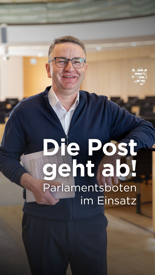 Botenmeister Jürgen Haeder ist im Bild zu sehen. Er hat Unterlagen unter den Arm geklemmt und lächelt in die Kamera. Im Hintergrund unscharf zu erkennen ist der Plenarsaal des Landtages. Der folgende Schriftzug ist zu lesen: "Die Post geht ab! Parlamentsboten im Einsatz"
