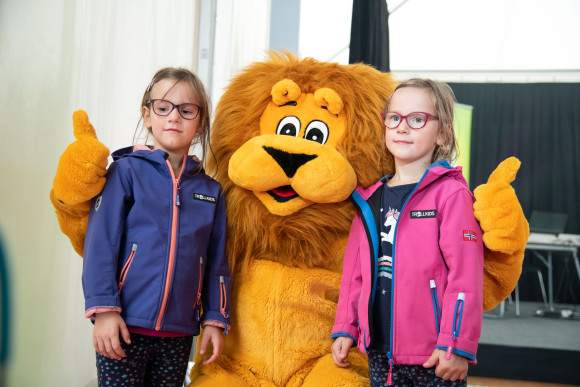 Ein Löwen-Maskottchen steht mit zwei Kindern zusammen und posiert für eine Kamera.