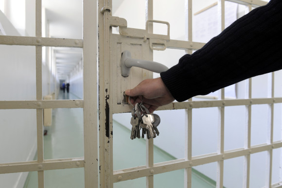 Eine Person schließt ein Gittertor in einer Vollzugsanstalt auf.