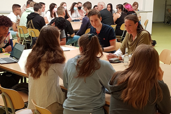 Schülerinnen und Schüler sitzen an einem Tisch zusammen und reden miteinander.