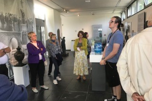 Gruppe der ehemaligen Abgeordneten stehen in einem Museum und hören einem Museumsführer zu.