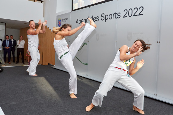 Drei Sportler und Sportlerinnen demonstrieren eine Kampfsportchoreographie.