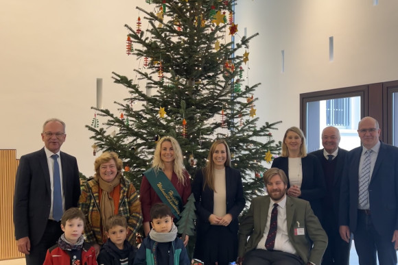 Landtagspräsidentin Astrid Wallmann, Mitarbeitende des Landtages und Kinder stehen vor einer hohen Tanne, die weihnachtlich geschmückt wurde.