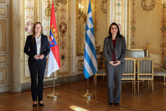 Landtagspräsidentin Astrid Wallmann steht neben der Generalkonsulin Ioanna Kriebardi aus Griechenland. Im Hintergrund sind die Fahnen Hessens und Griechenlands.