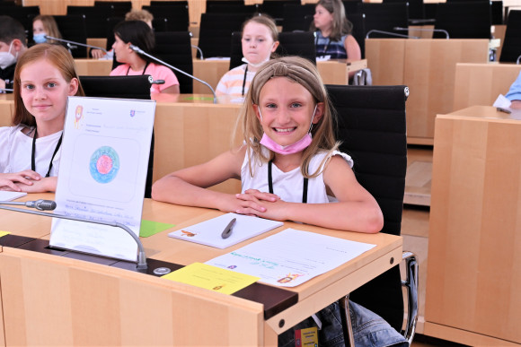 Eine Grundschülerin präsentiert beim Planspiel "Der Kinder-Landtag" stolz das selbst gemalte Logo ihrer Fraktion.