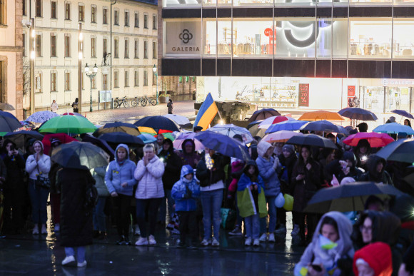 Mehrere Menschen stehen mit Regenschirmen und Flagen der Ukraine zusammen.