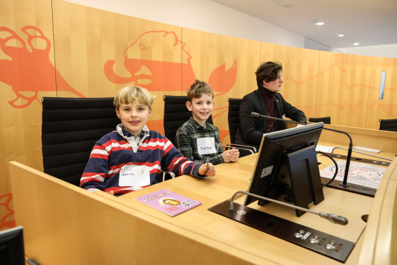 hess.landtag-foto-hupfeld-6220.jpg Zwei Kinder und ein Gästeführer sitzen im Präsidium