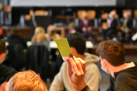 Ein Schüler hält bei einer Dialogveranstaltung mit Abgeordneten eine grüne Abstimmungskarte hoch.