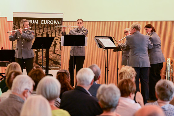 Flötistinnen des Heeresmusikkorps Kassel stehen vor Publikum auf einer Bühne und spielen von Notenblättern ab.