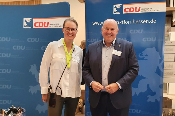 Zwei Parteimitglieder der CDU stehen vor einer Stellwand der CDU.