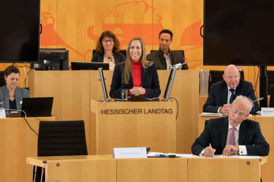 Astrid Wallmann steht am Podium des Hessischen Landtages. Neben, hinter und vor ihr sitzen weitere Abgeordnete.