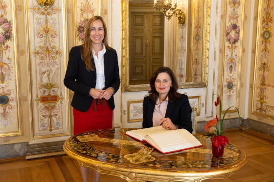 Landtagspräsidentin Astrid Wallmann steht neben der Generalkonsulin des Staates Israel. Diese sitzt an einem Tisch und schreibt in das Gästebuch.