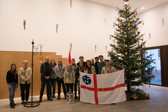 Eine große Pfadfindergruppe bei der Übergabe des Friedenslichts in den Räumlichkeiten des Hessischen Landtags vor einem Weihnachtsbaum. Weiterhin zu sehen ist eine Flagge.