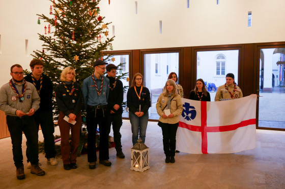 Eine Pfadfindergruppe bei der Übergabe des Friedenslichts in den Räumlichkeiten des Hessischen Landtags vor einem Weihnachtsbaum.  Weiterhin zu sehen ist eine Flagge.