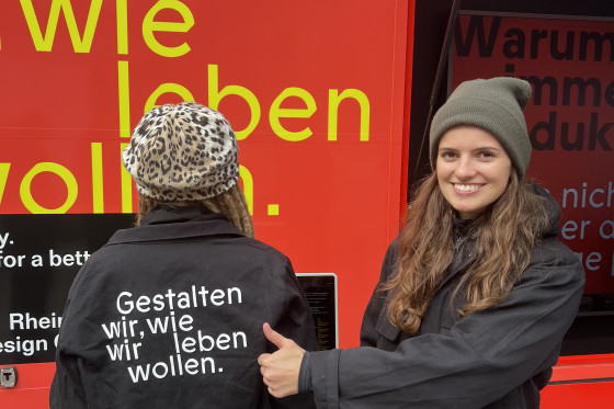 Zwei junge Frauen. Die linke trägt ein Kleidungsstück mit der Aufschrift "Gestalten wir, wie wir leben wollen."