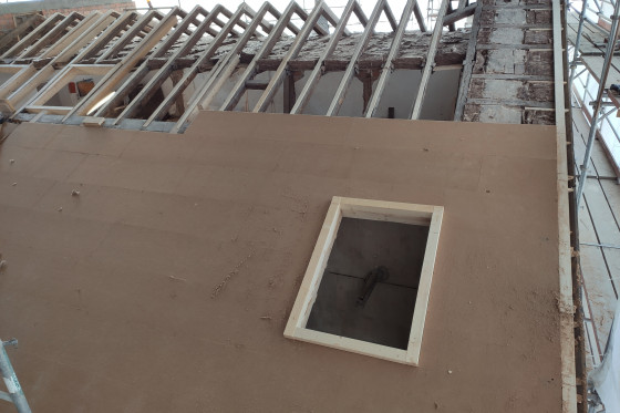 Ein halb fertiges Dach in dem ein Fensterrahmen platziert ist.