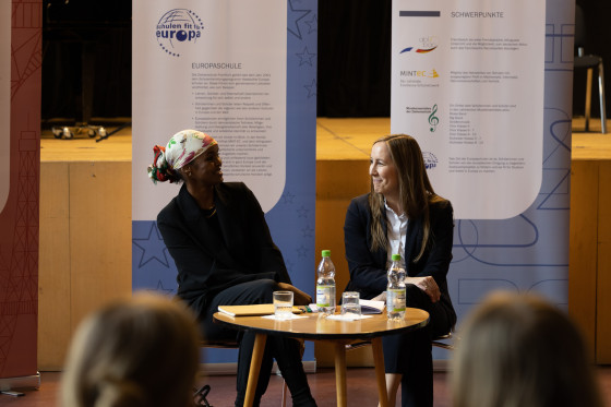  Landtagspräsidentin Astrid Wallmann und die Preisträgerin des Hessischen Friedenspreises Ilwad Elman sitzen an einem kleinen Tisch in der Aula der Ziehenschule.