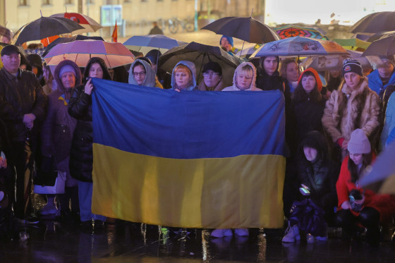 Mehrere Menschen stehen zusammen und halten eine große ukrainische Flagge hoch.