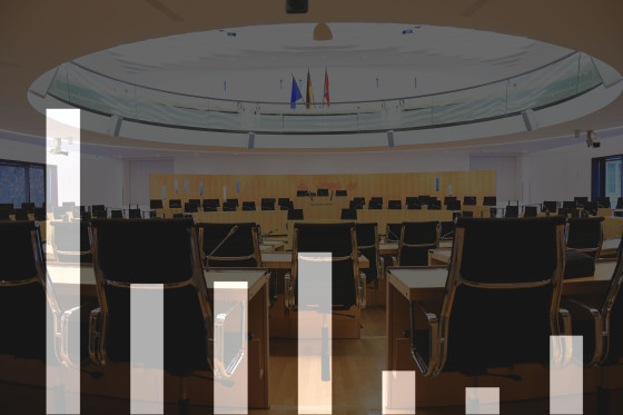 Symbolbild: Ausgegraute Säulengrafik ohne Zahlen vor verdunkeltem Hintergrund des Plenarsaals im Landtag