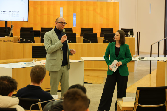 Mann spricht in Mikrofon neben der Moderatorin