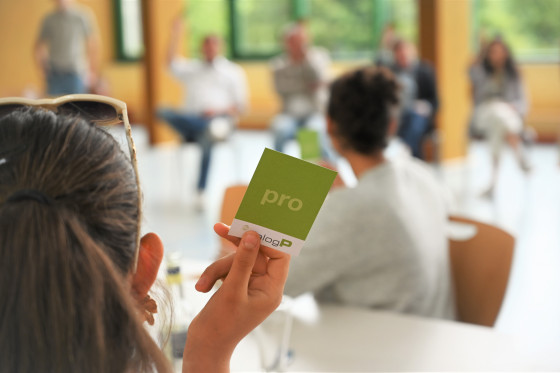 Eine Schülerin hält eine grüne Karte mit der Aufschrift "Pro" in die Luft.