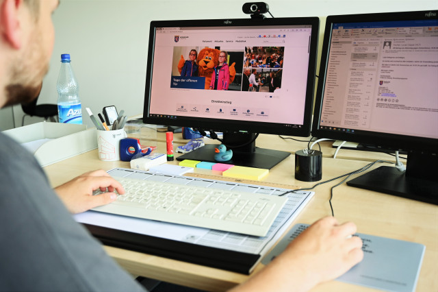 Ein junger Mann sitzt an einem Schreibtisch und arbeitet am Computer. Geöffnet ist die Website des Hessischen Landtages.